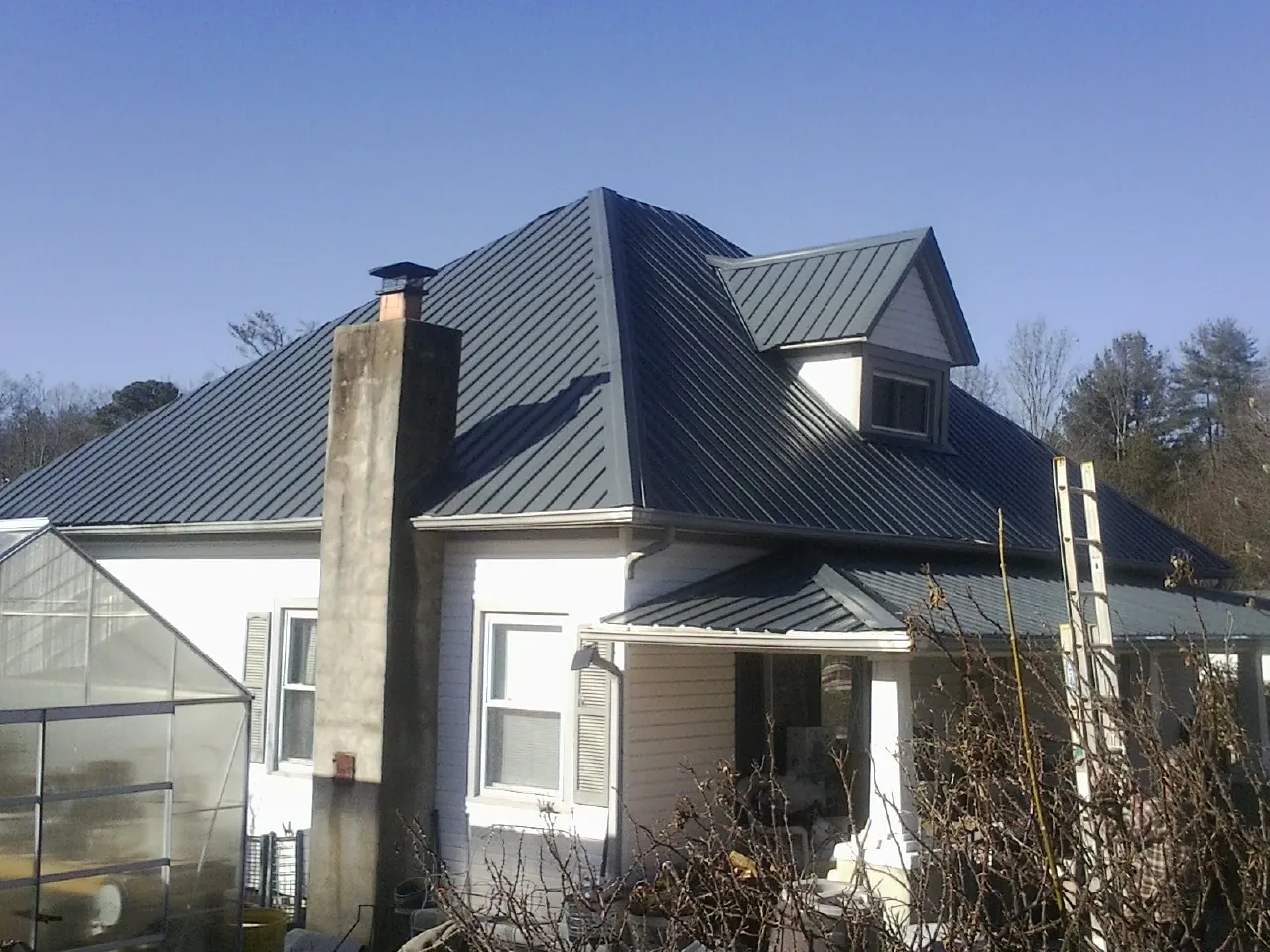Dark blue standing seam metal roof on a white farmhouse with dormer — Slate & Tile Roof Repair by Roofing Brothers in Nickerson