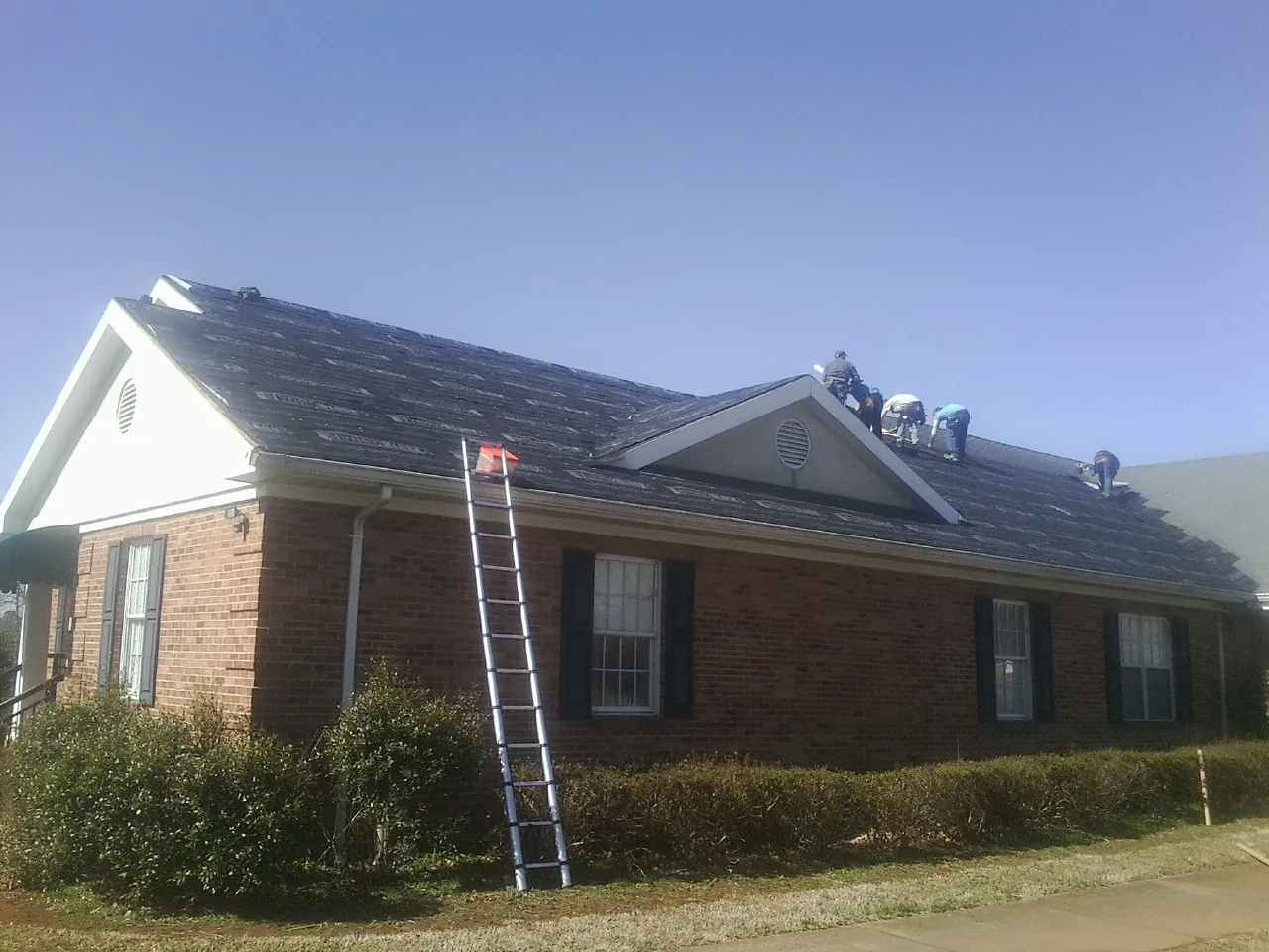 Crew tearing shingles off a brick ranch roof with a ladder set — Emergency Roof Repair work by our crew in Nickerson