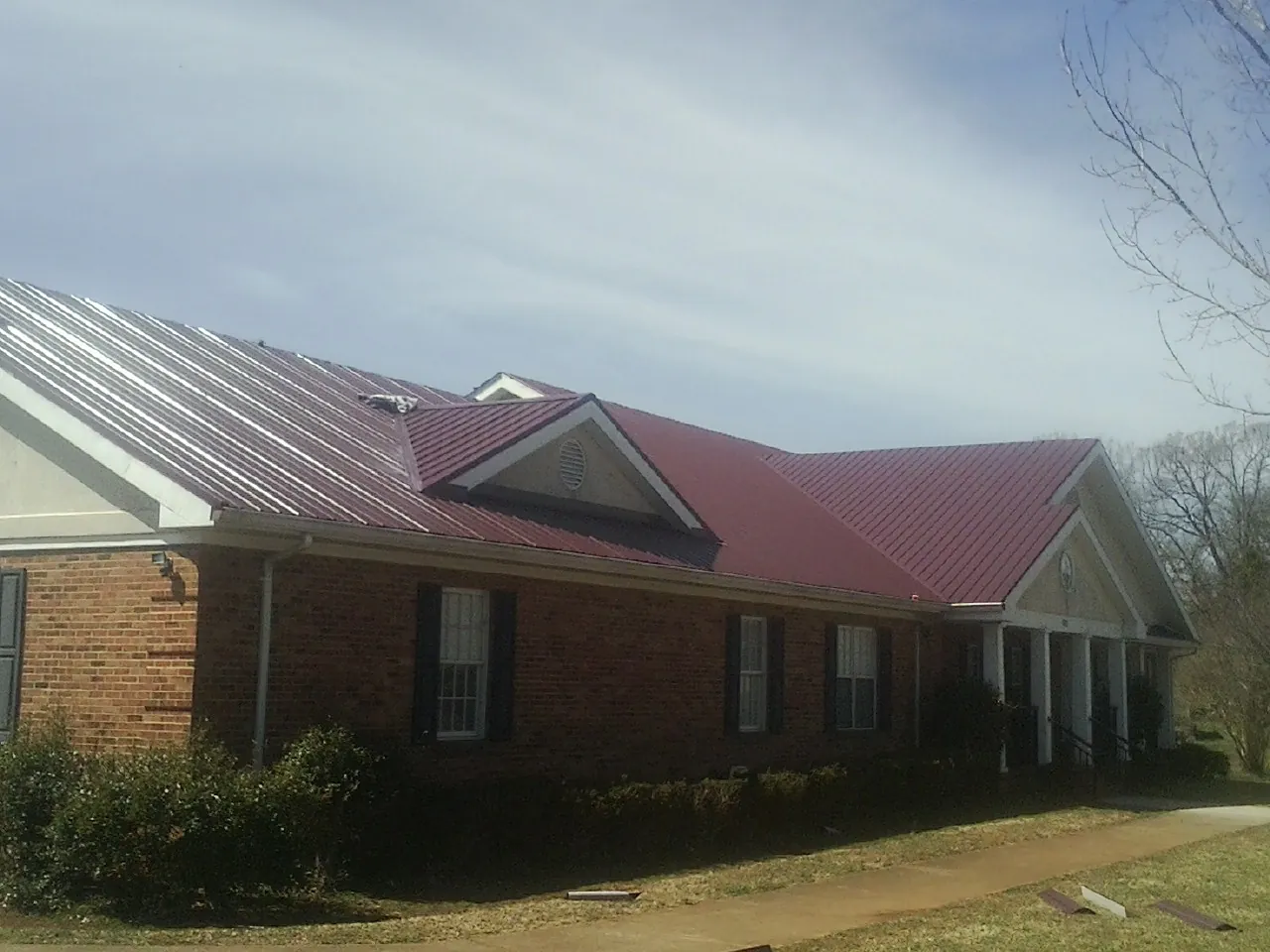 Red metal roof with gabled entries on a long brick building, from a Hail Damage Roof Repair job in Nickerson