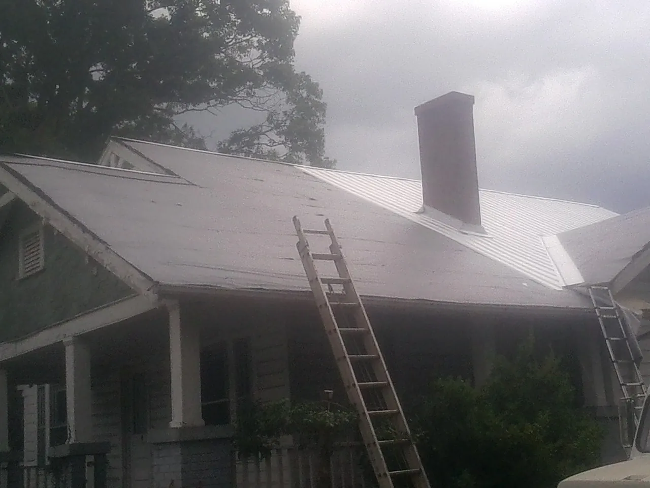 Ladders against a metal roof on an older home with a brick chimney in Nickerson