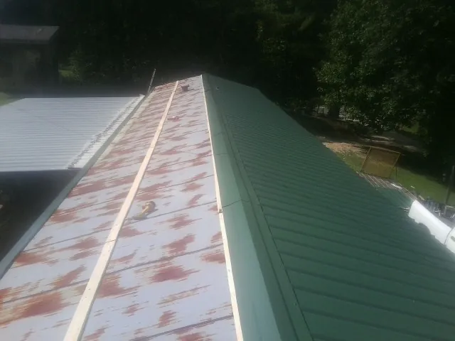 Old rusted panels beside newly installed green metal roofing — Wind Damage Roof Repair by Roofing Brothers in Nickerson