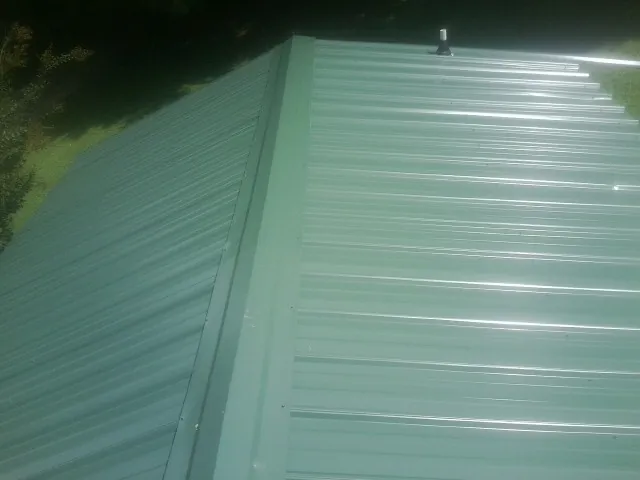 New green metal panels meeting at the ridge of a roof — Flat Roof Repair work by our crew in Nickerson