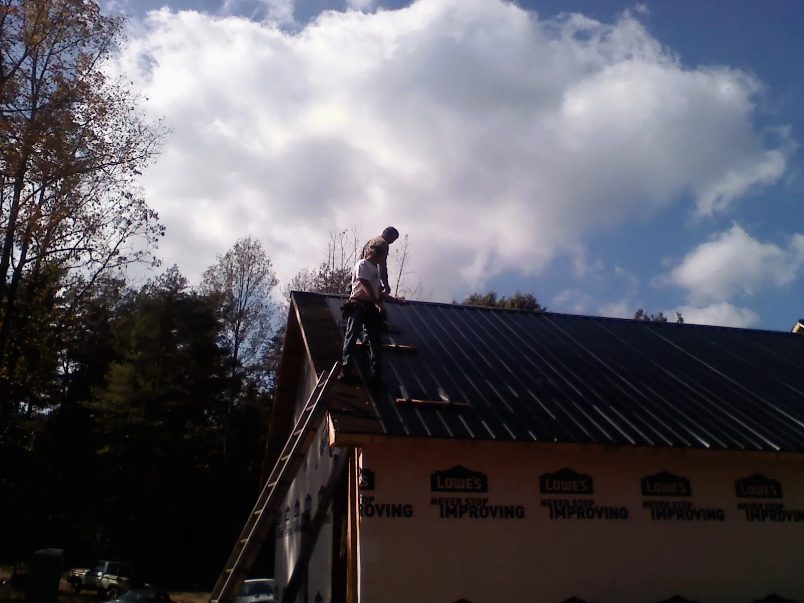Roofer fastening dark metal panels high against a cloudy sky, from a Roof Inspection job in Nickerson