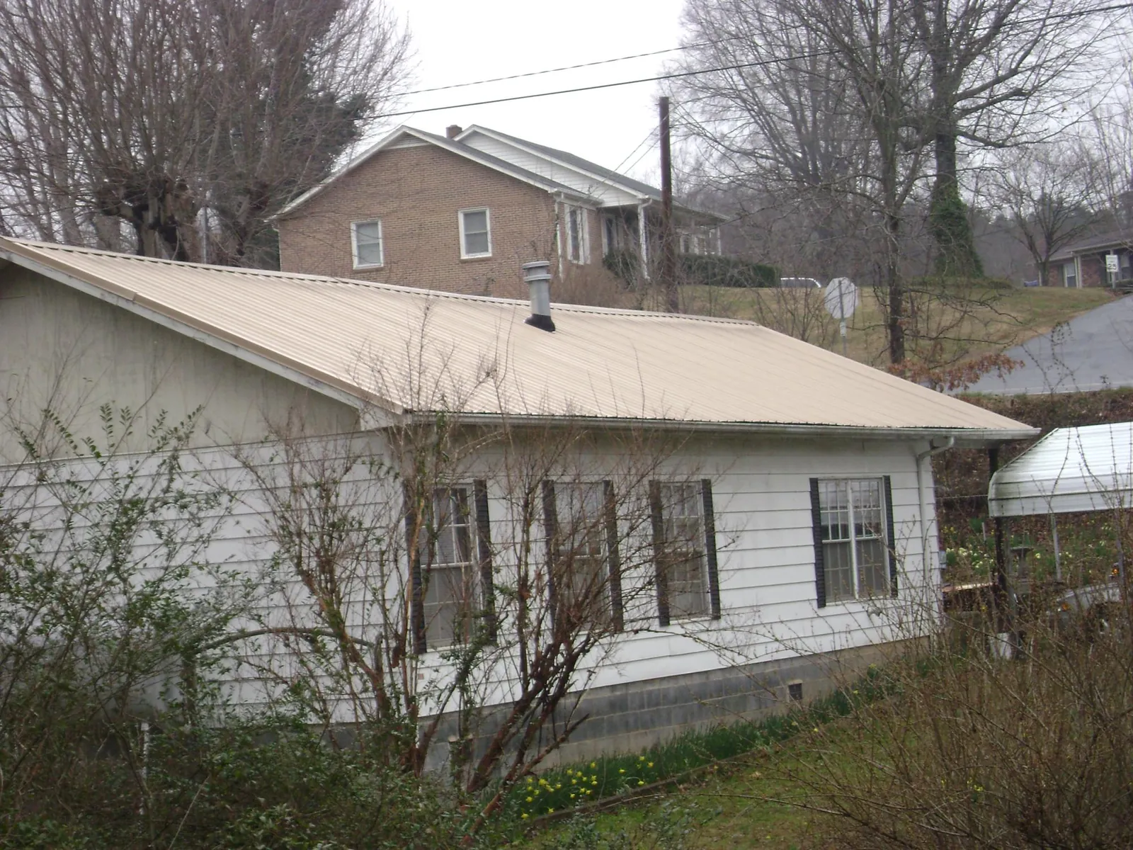 Tan metal roof on a white sided house set into a hillside — Commercial Roofing by Roofing Brothers in Nickerson