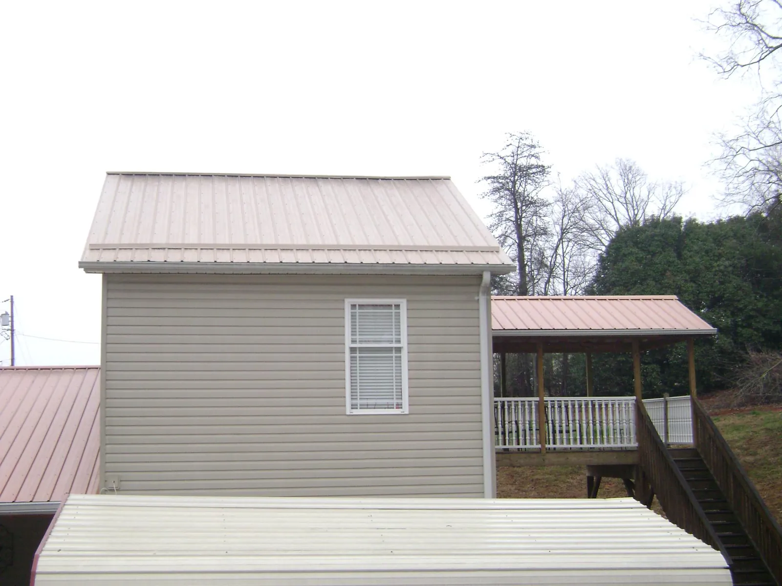 Tan metal roofs on a two story addition and attached porch, from a Roof Replacement job in Nickerson